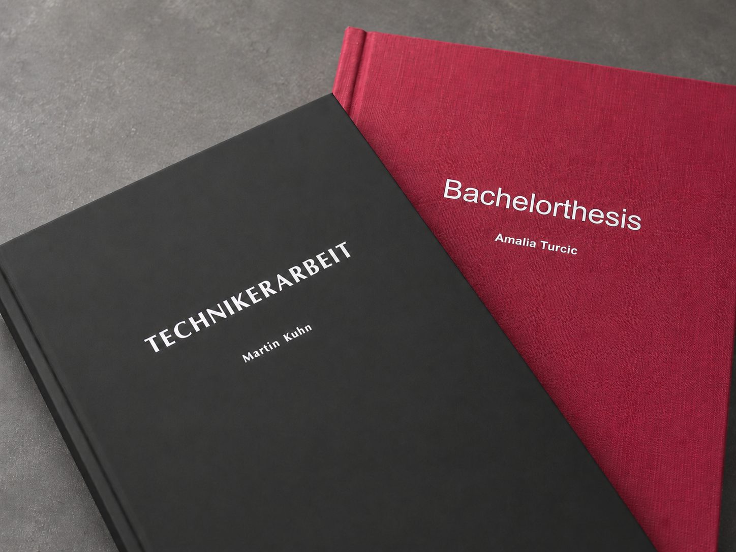 Schwarze Technikerarbeit mit Silberprägung neben roter Bachelorthesis mit Prägedruck